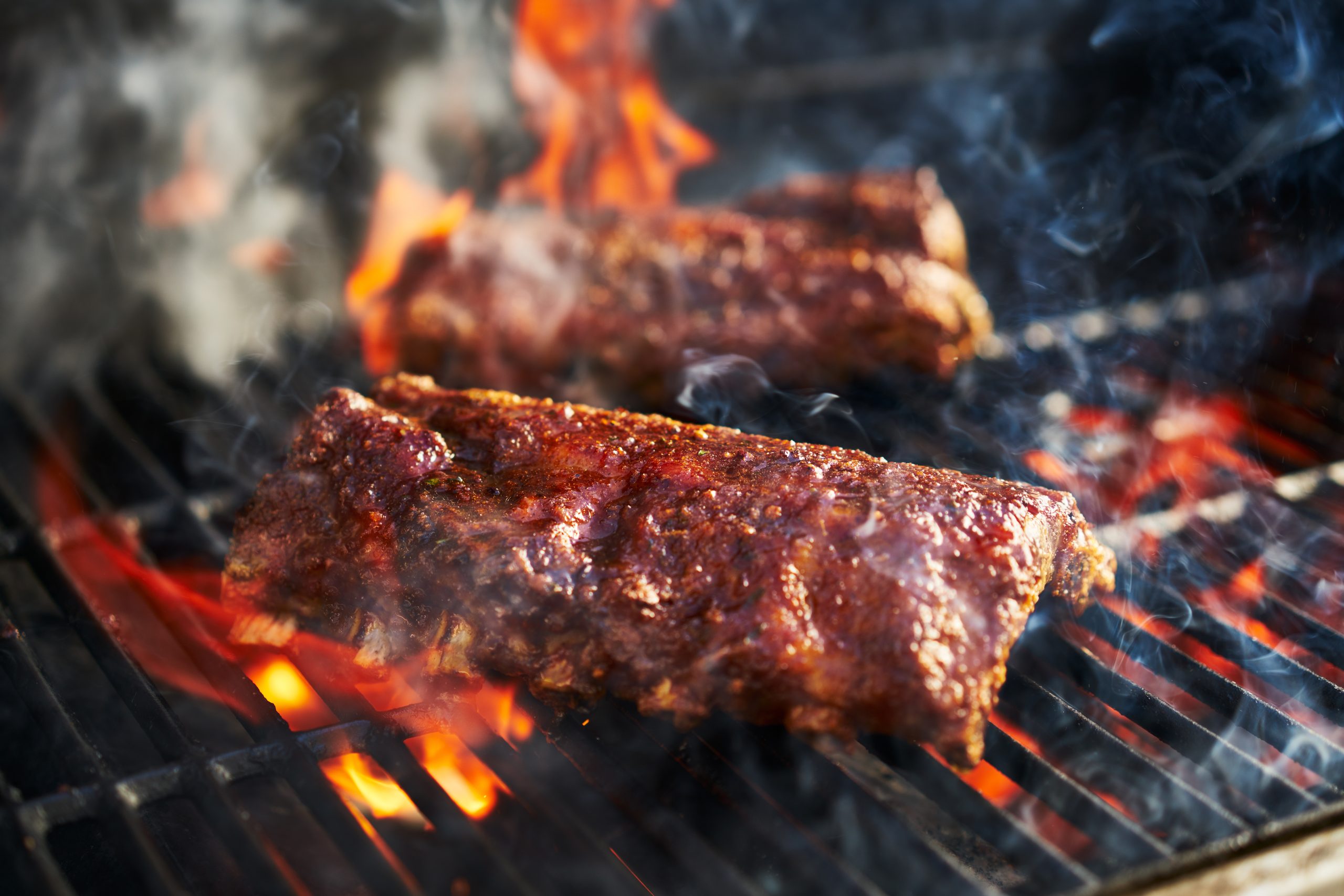 smoky barbecue ribs sizzle over an open flame, sauce caramelizing as fire flickers beneath the grill in true Texas cookout style